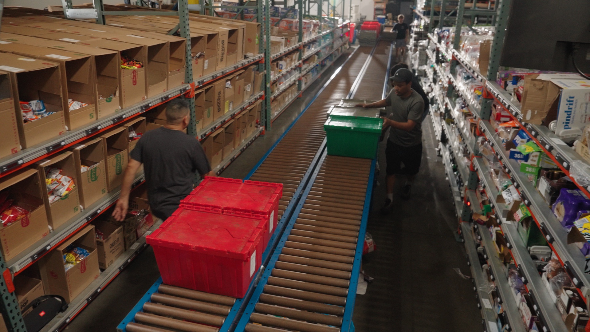 Warehouse team members moving delivery totes along a conveyor between picking aisles
